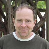 A man standing in front of wooden beams and greenery outside.