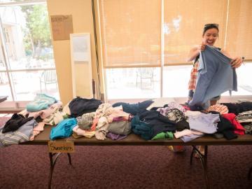 A student smiling as they pick up a shirt from a table of clothes