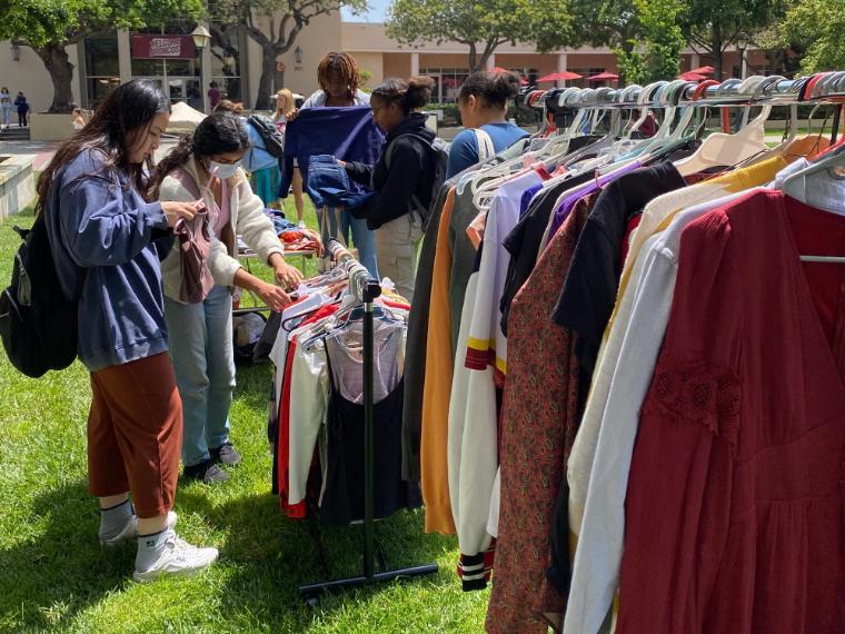 Close up of a clothing rack outside with people shopping at a table in the background
