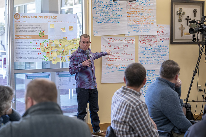 a person speaking into a hand-held microphone in front of a hand-written flip-chart