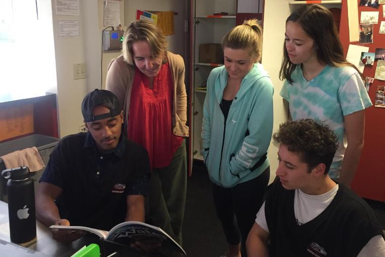 A group of students and staff looking at a booklet in an office