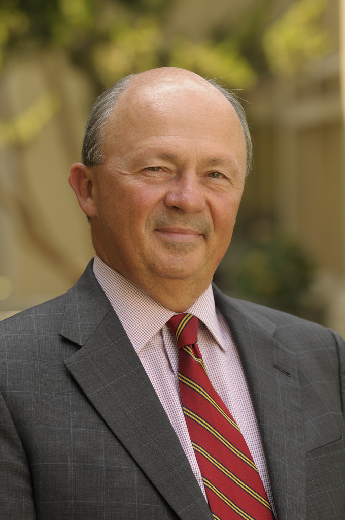 A well-dressed man in a suit and red tie smiling.