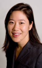 A person smiling, wearing a dark jacket against a plain background.