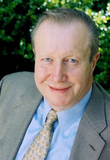 A person in a suit smiles in front of a leafy background. image link to story