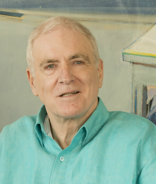 A man in a bright blue shirt is indoors, smiling. image link to story