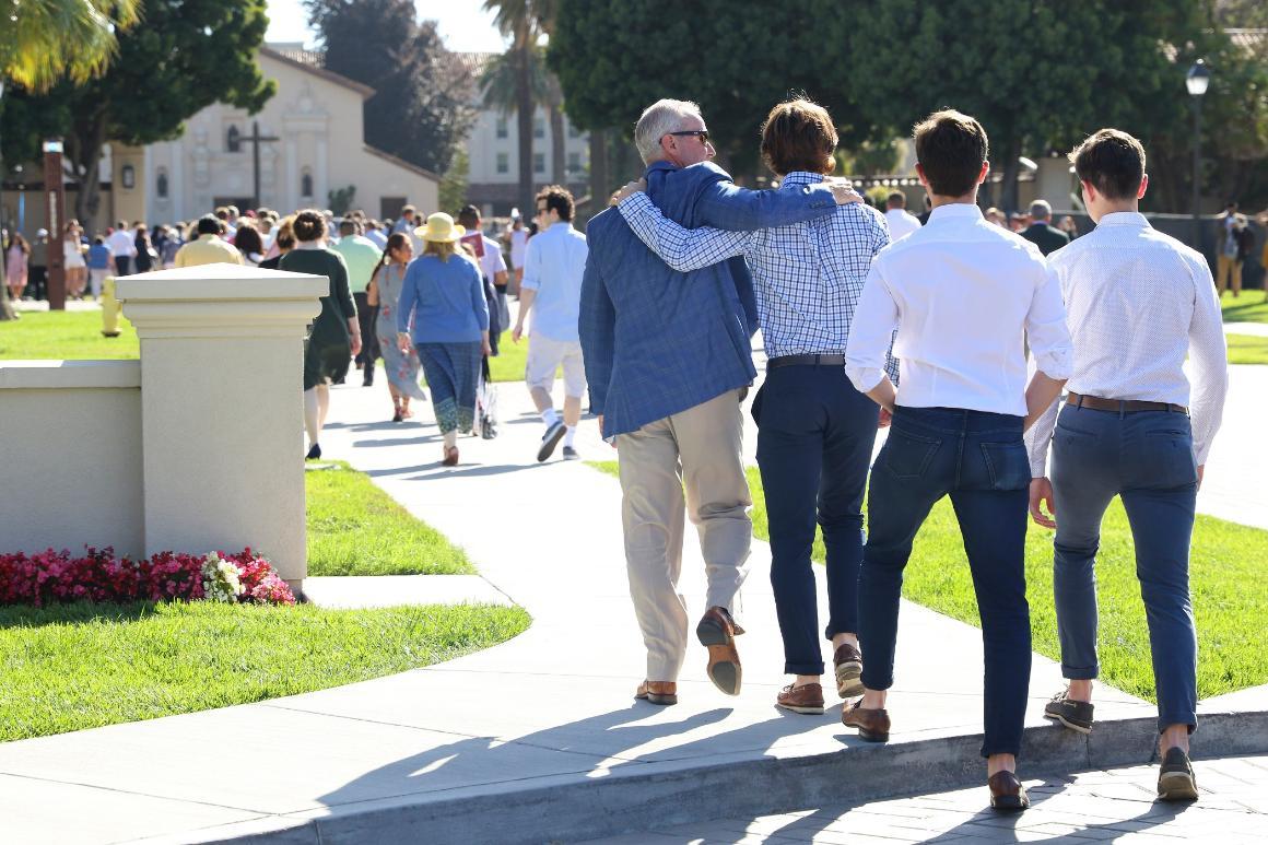 A large group of people with men in the foreground are walking towards the Mission Church.