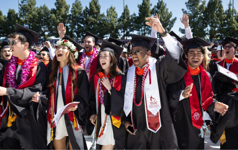 A group of students standing and cheering at a commencement ceremony
