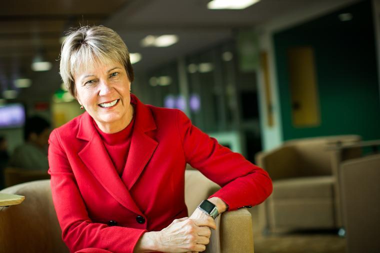 A person in a red jacket smiling in an office or lounge area.