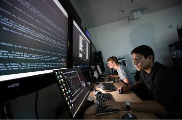 Two male students staring at their laptops in a dark room. 