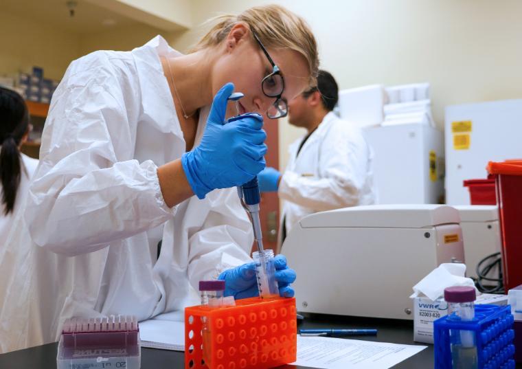 Woman bioengineering student uses a syringe to fill a vile during a bioengineering lab.