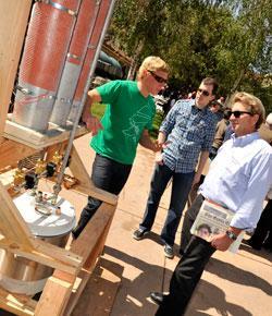Three people examine a repurposed wooden object outdoors.