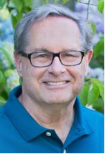 A person smiling with a blurred leafy background.