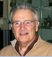 A man wearing glasses and a beige sweater, standing indoors.