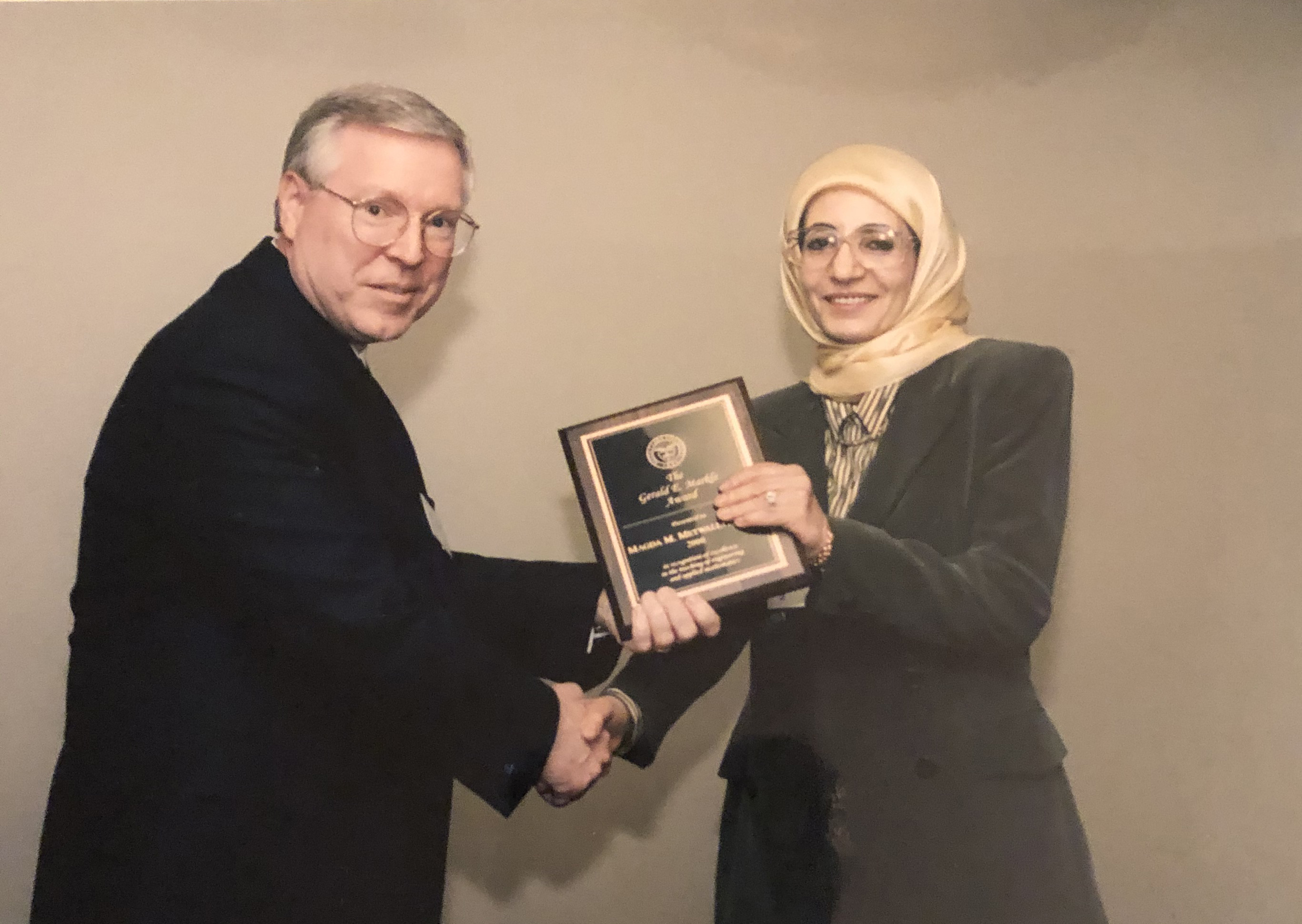 Two people exchange a trophy in a formal setting.