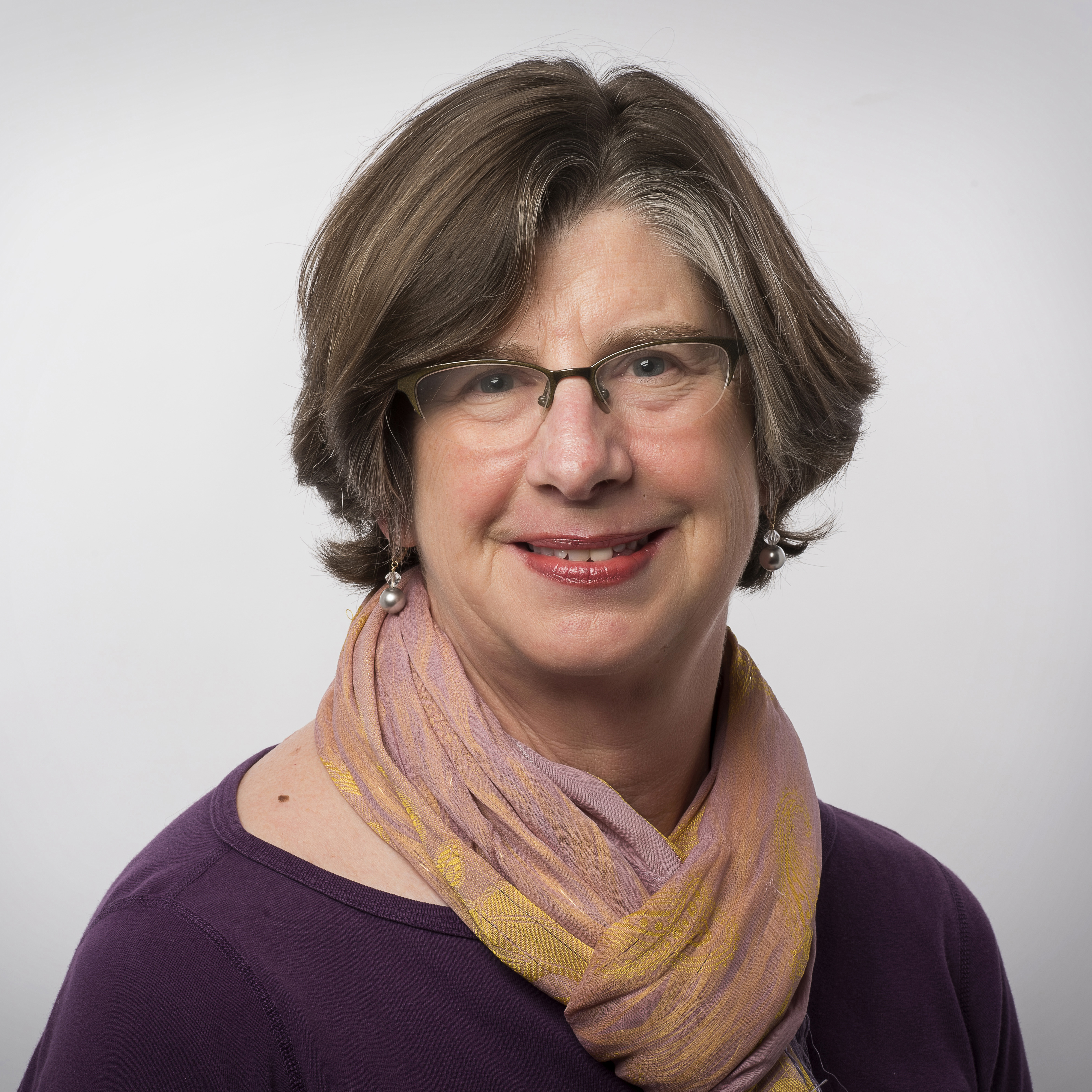 A person wearing glasses and a scarf, smiling at the camera. image link to story