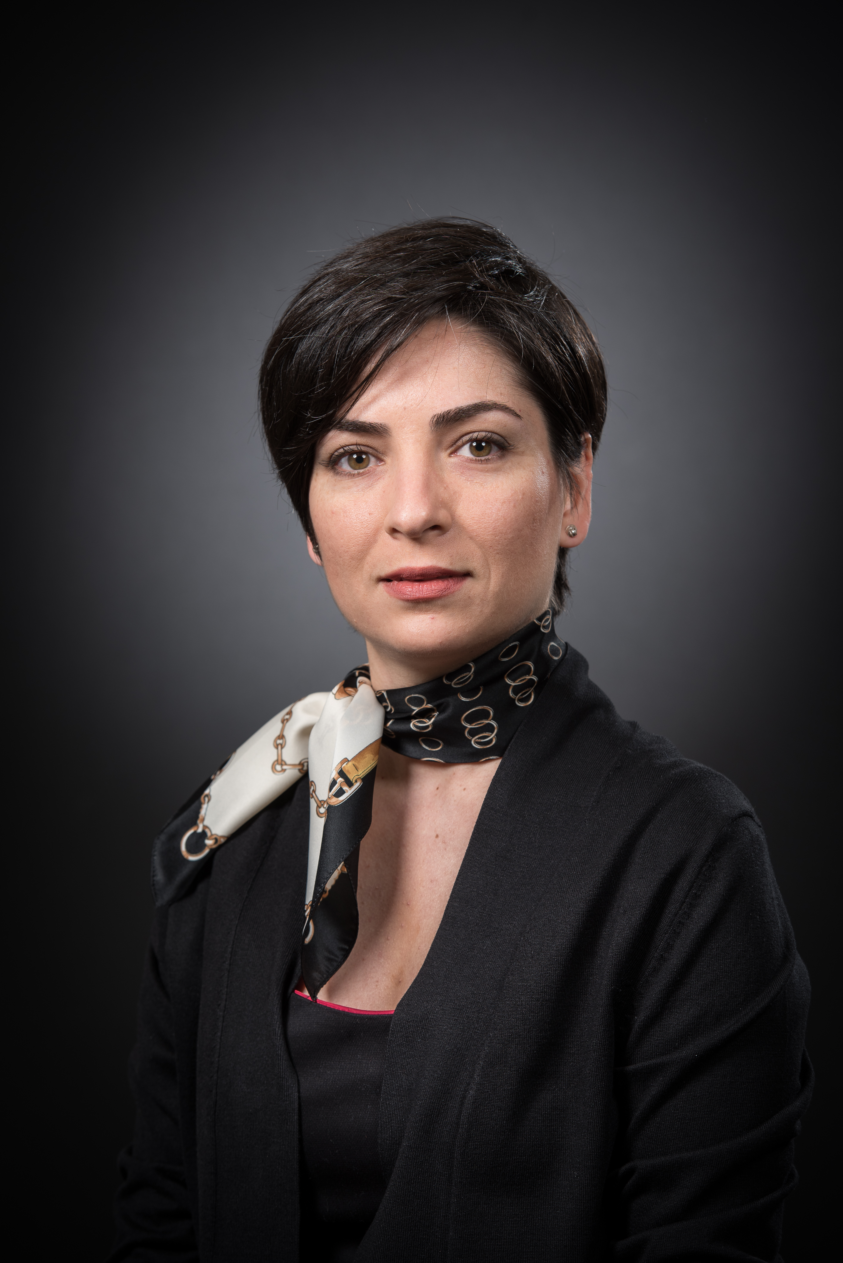 A person in formal attire with a dark background.