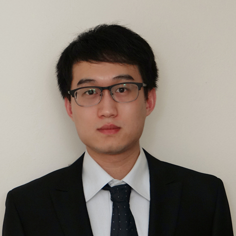 A person wearing glasses, a black suit, white shirt, and a dark tie.