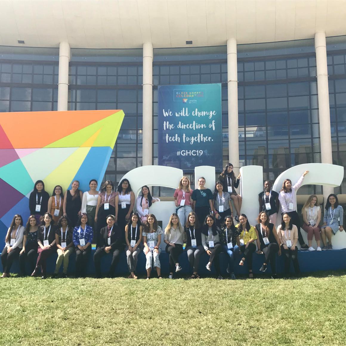 SCU students at Grace Hopper Conference 2019 in front of banner reading "We will change the direction of tech together"