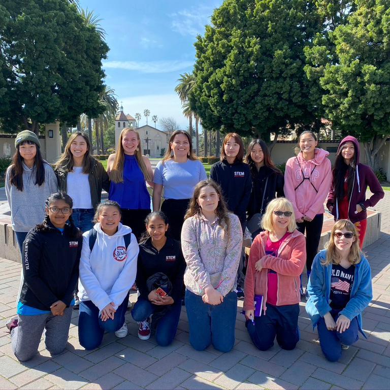 Three SWE officers and 11 middle school girls pose for a photo in front of a fountain at Santa Clara University