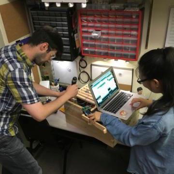 Two people work together at a table with electronic equipment.