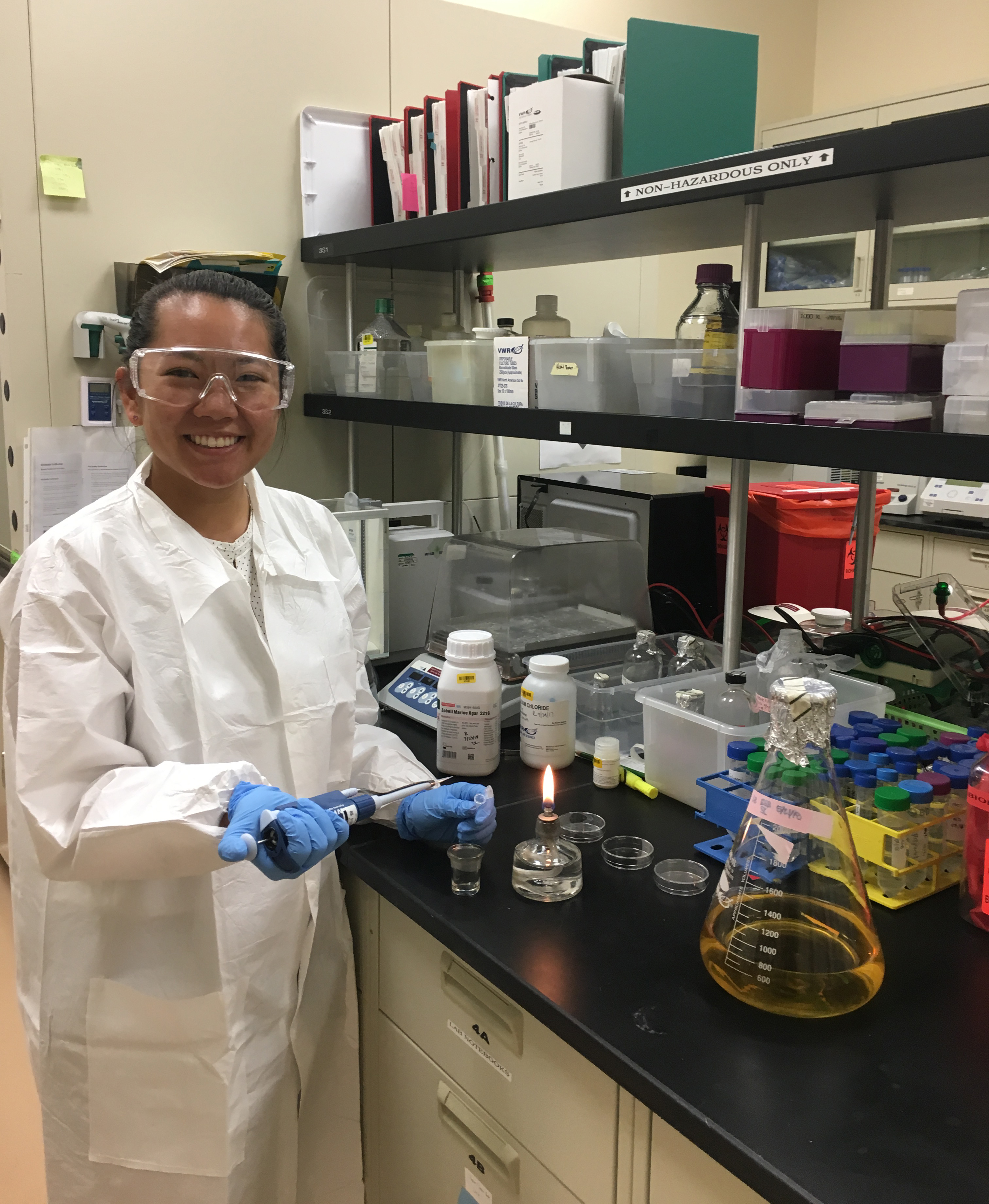 Person in a laboratory holding blue gloves and a beaker in 'Goo Portrait'. image link to story