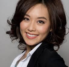 A woman smiling wearing a white shirt and black blazer.