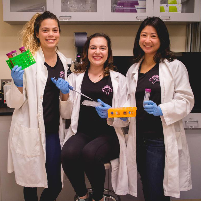 Three people in lab coats holding colorful lab samples smiling.