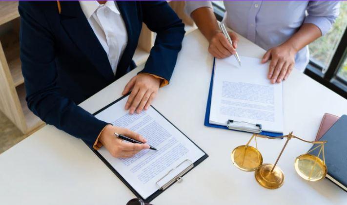 stock image showing a desk with scales of justice and two sets of hands working on editing documents 