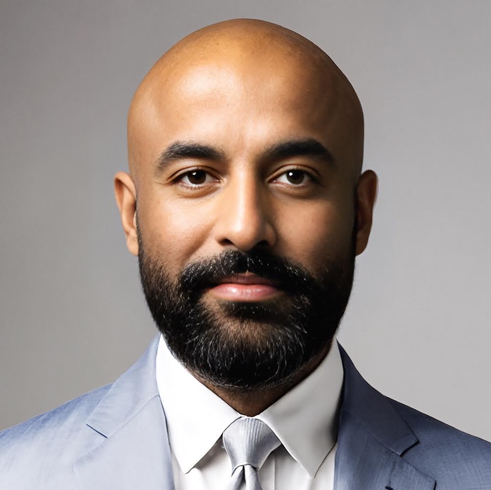 professor Pav Athwal a man with a shaved head and full black beard wearing a light blueish grey suit and a white collared shirt and grey tie