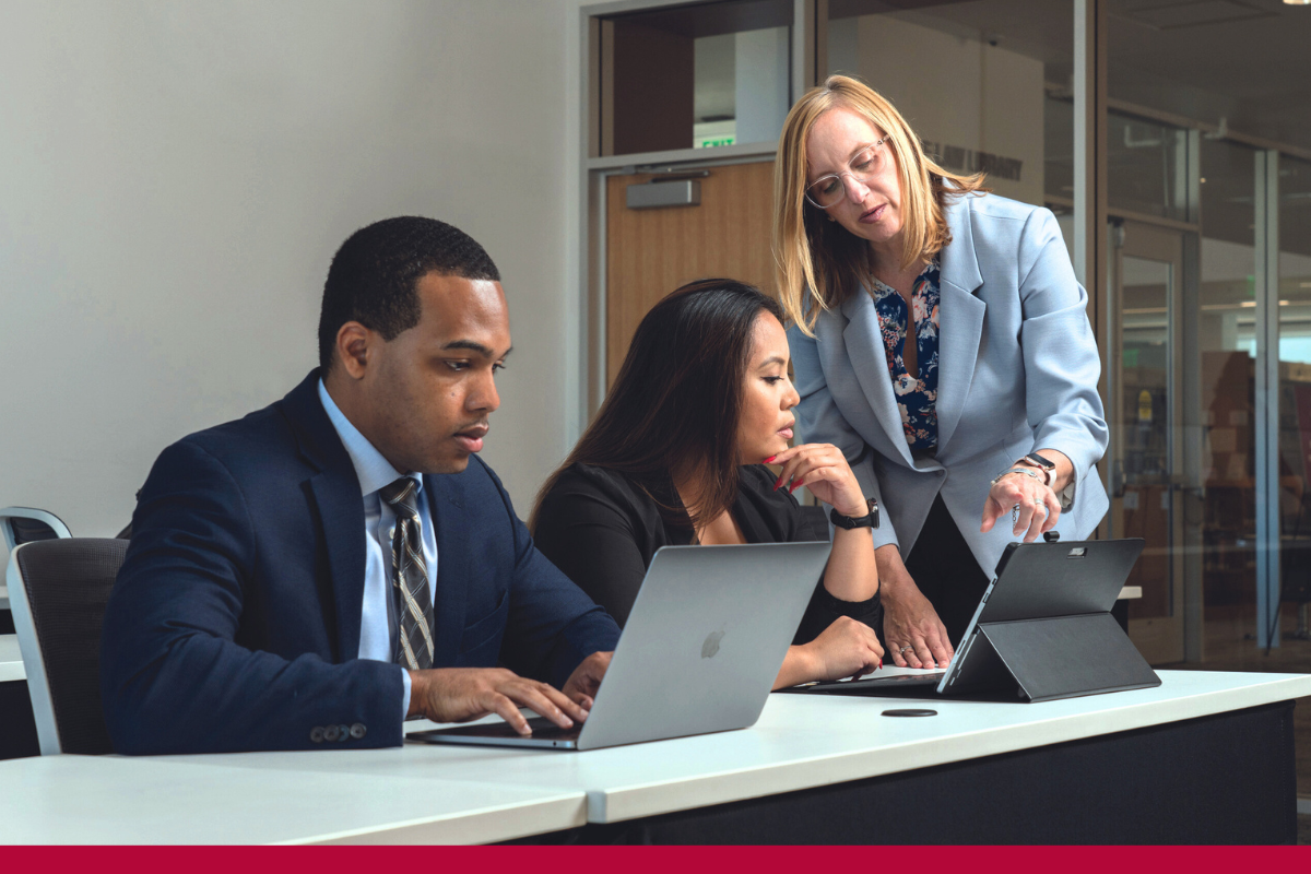 Professor instructing two Law students on laptops. 